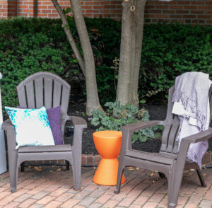 Two gray chairs with pillows under a shaded tree in a brick courtyard